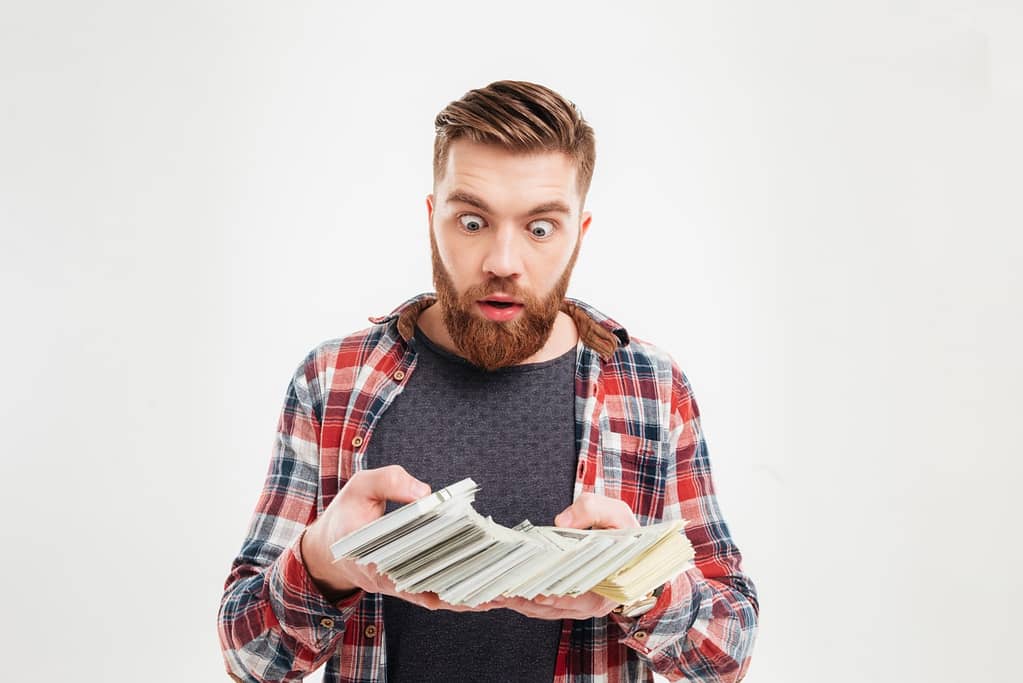 A bearded man flaunting his infinite wealth while holding a stack of money on a white background.