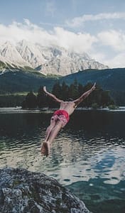 A man jumping into a lake with mountains in the background.