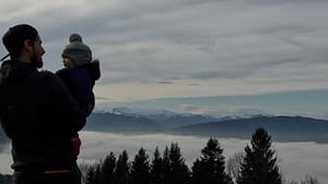 A man holding a child in front of a mountain with clouds in the background.