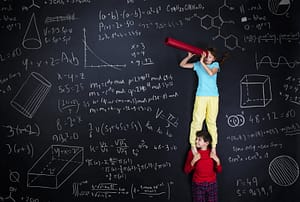 Two kids' financial literacy while standing in front of a blackboard with formulas written on it.