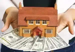 A woman holding a house model and money in her hands.