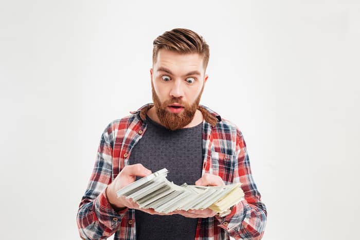 A bearded man flaunting his infinite wealth while holding a stack of money on a white background.