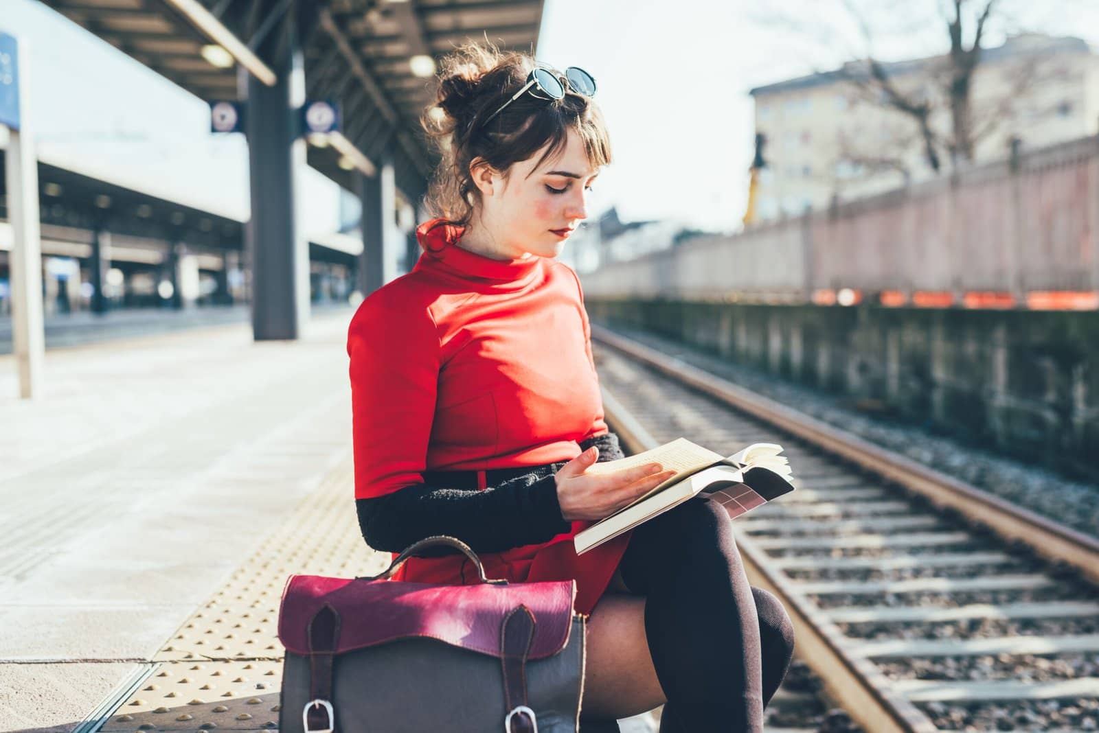 Photo of a young woman reading a book near train tracks
