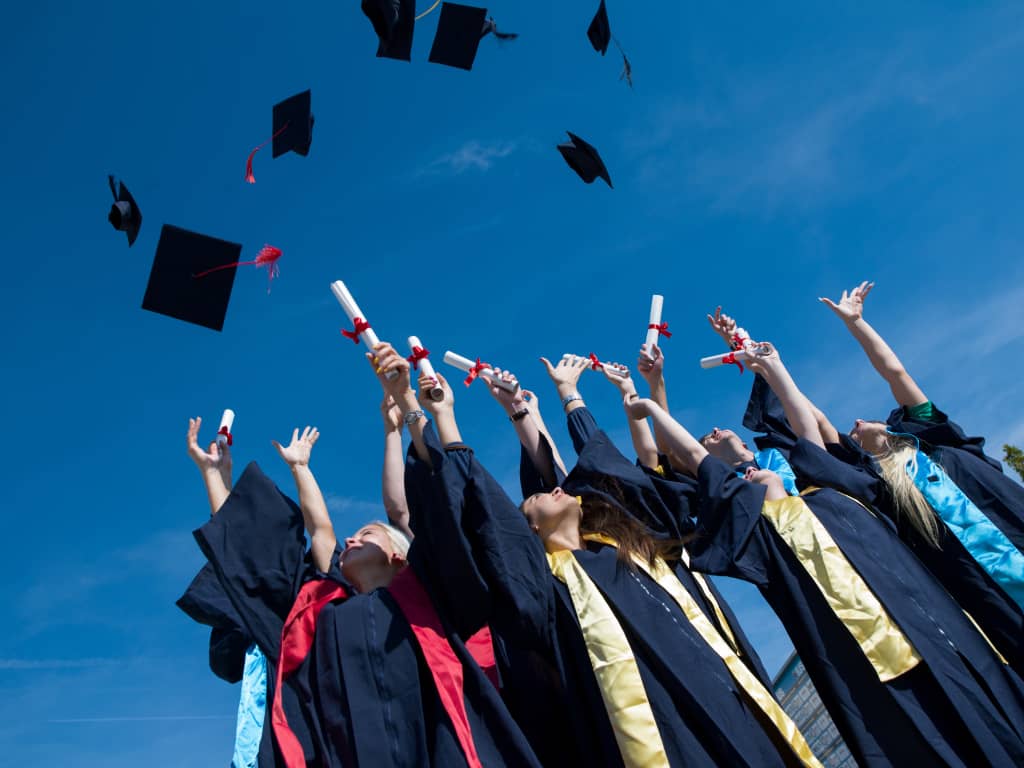 A group of graduates demonstrating their financial literacy by tossing their hats in the air.